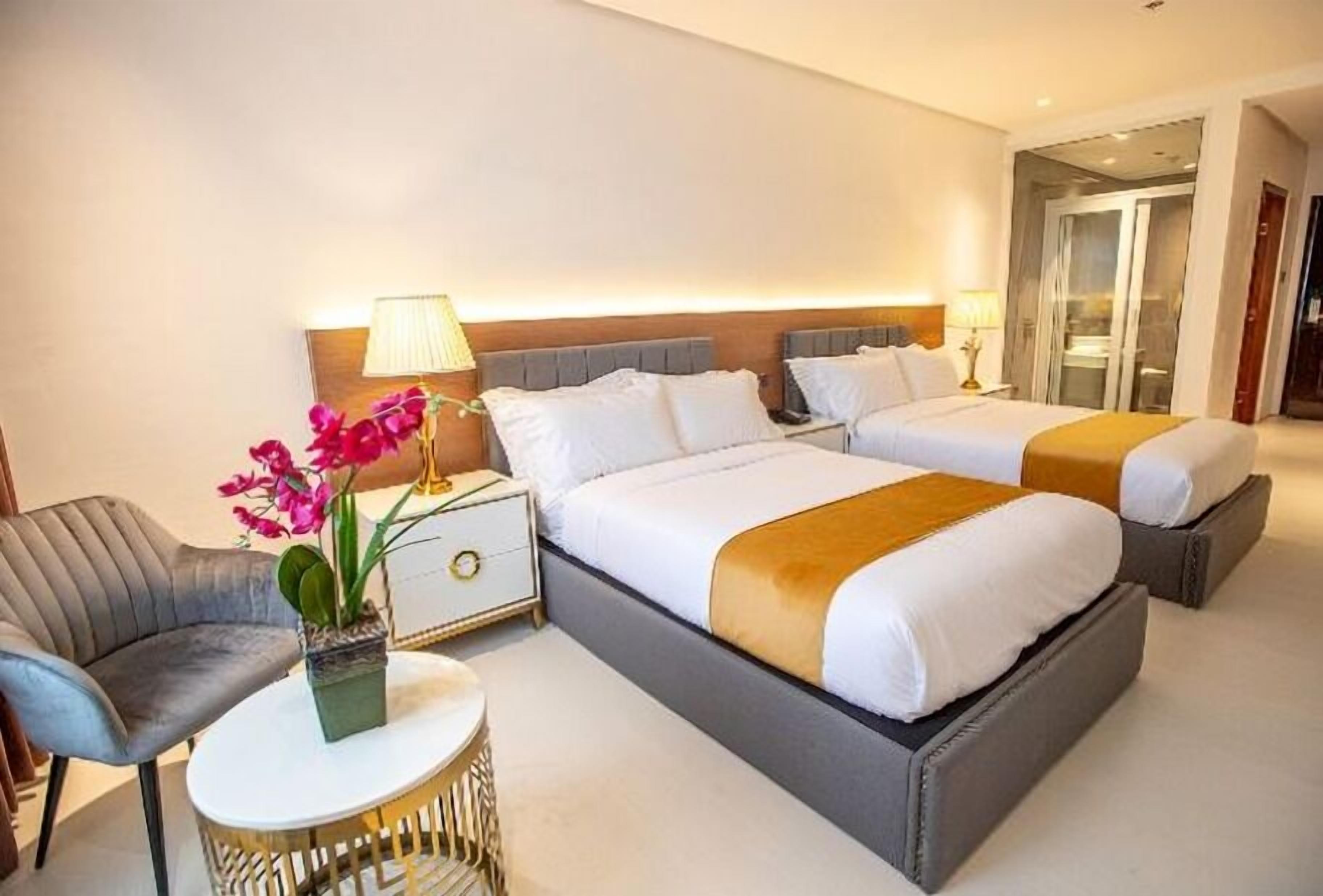 A hotel room with a large bed, bedside tables, a chair, and a small round table with a plant.