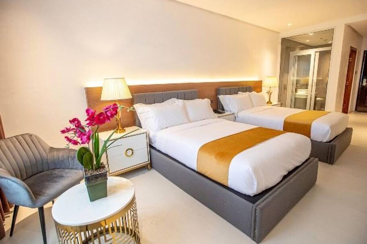 A hotel room with a large bed, bedside tables, a chair, and a small round table with a plant.