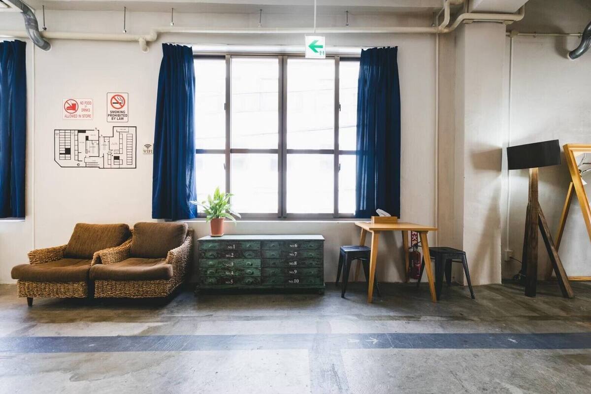 Ein Zimmer mit einer Couch, einem kleinen Tisch, einer Zimmerpflanze und einem Schrank. An den Wänden befinden sich Schilder, die darauf hinweisen, dass Essen und Getränke sowie Rauchen verboten sind.