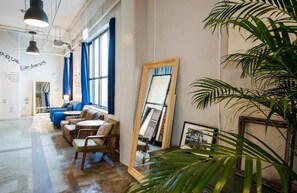 A spacious room with a large window, a blue sofa, a wooden chair, and a mirror on the wall. - Kalakaua Inn The Kitchen Hostel Ao (Naha)