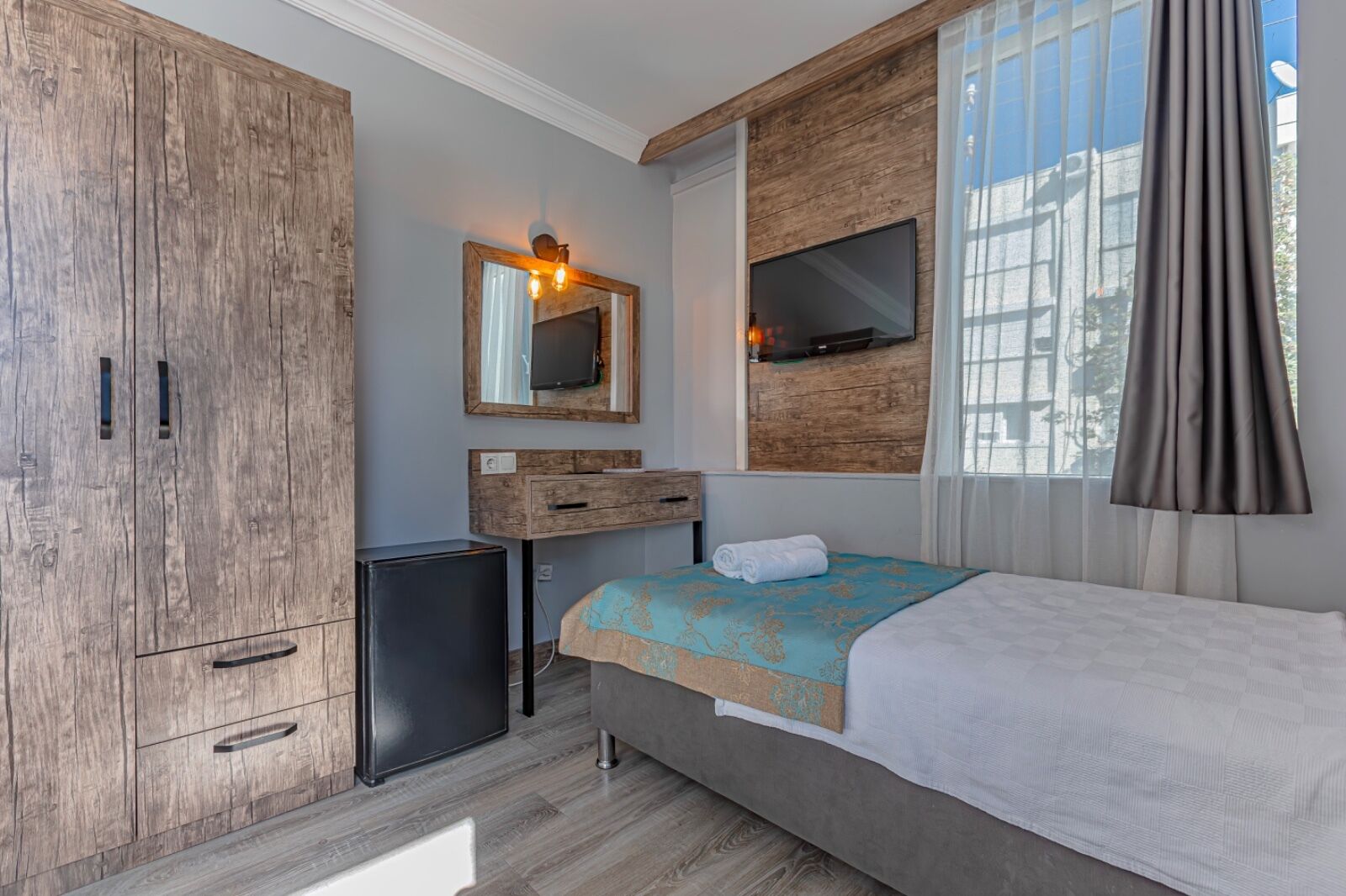 A bedroom with a bed, a wardrobe, a small desk, a mirror, and a TV mounted on the wall.