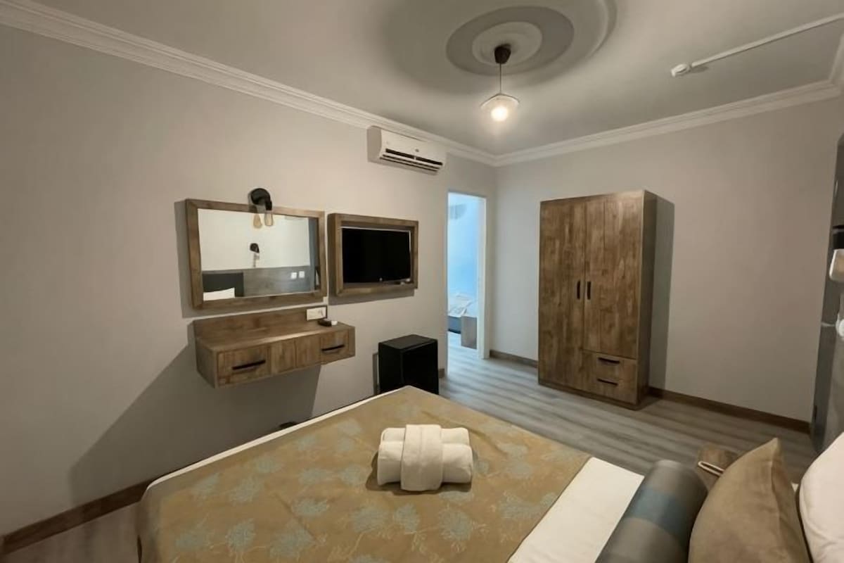 A hotel room with a bed, a TV, a mirror, a wardrobe, and an air conditioning unit.