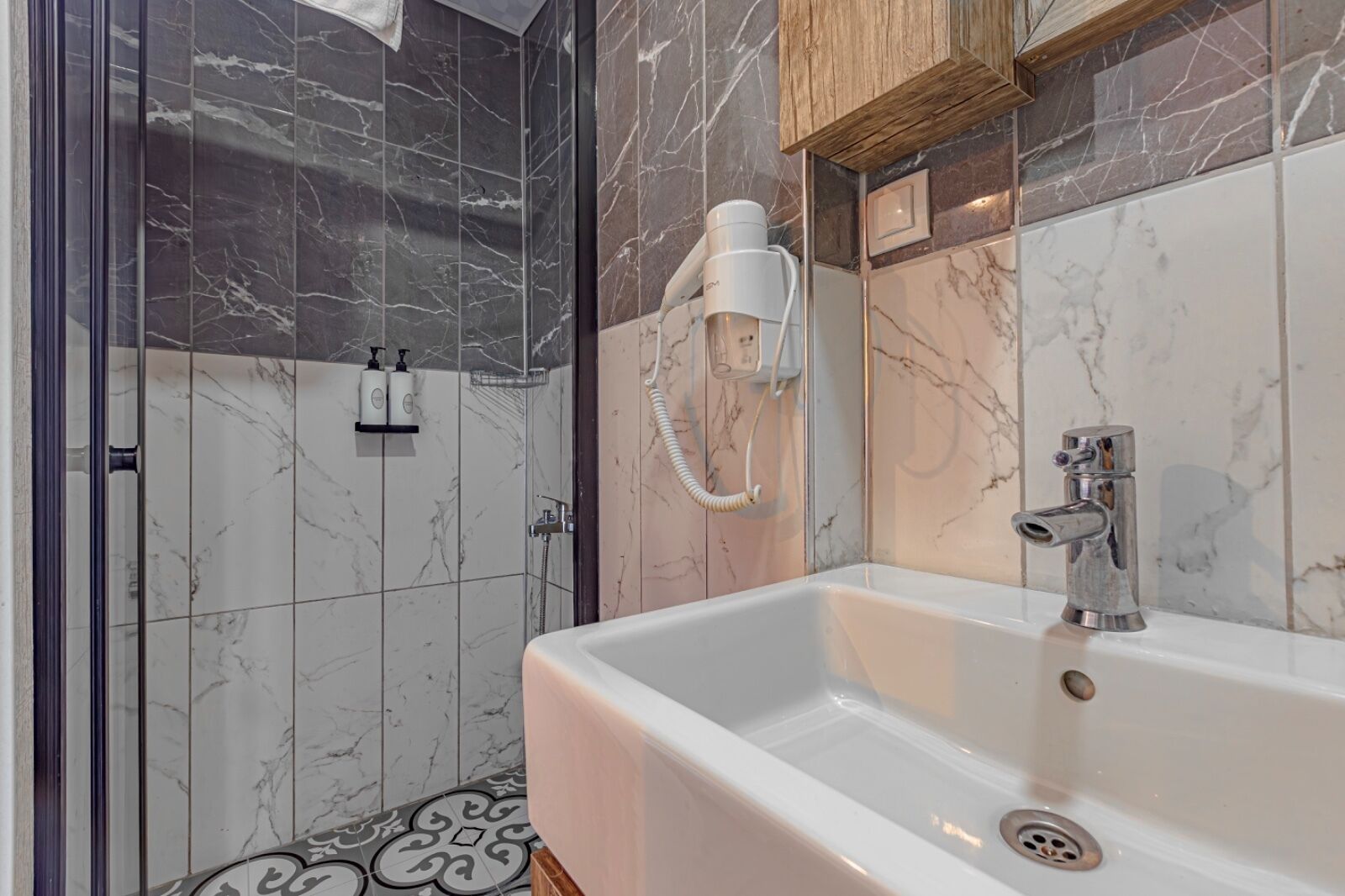 A modern bathroom with a large white sink, a handheld showerhead, and a glass-enclosed shower area.