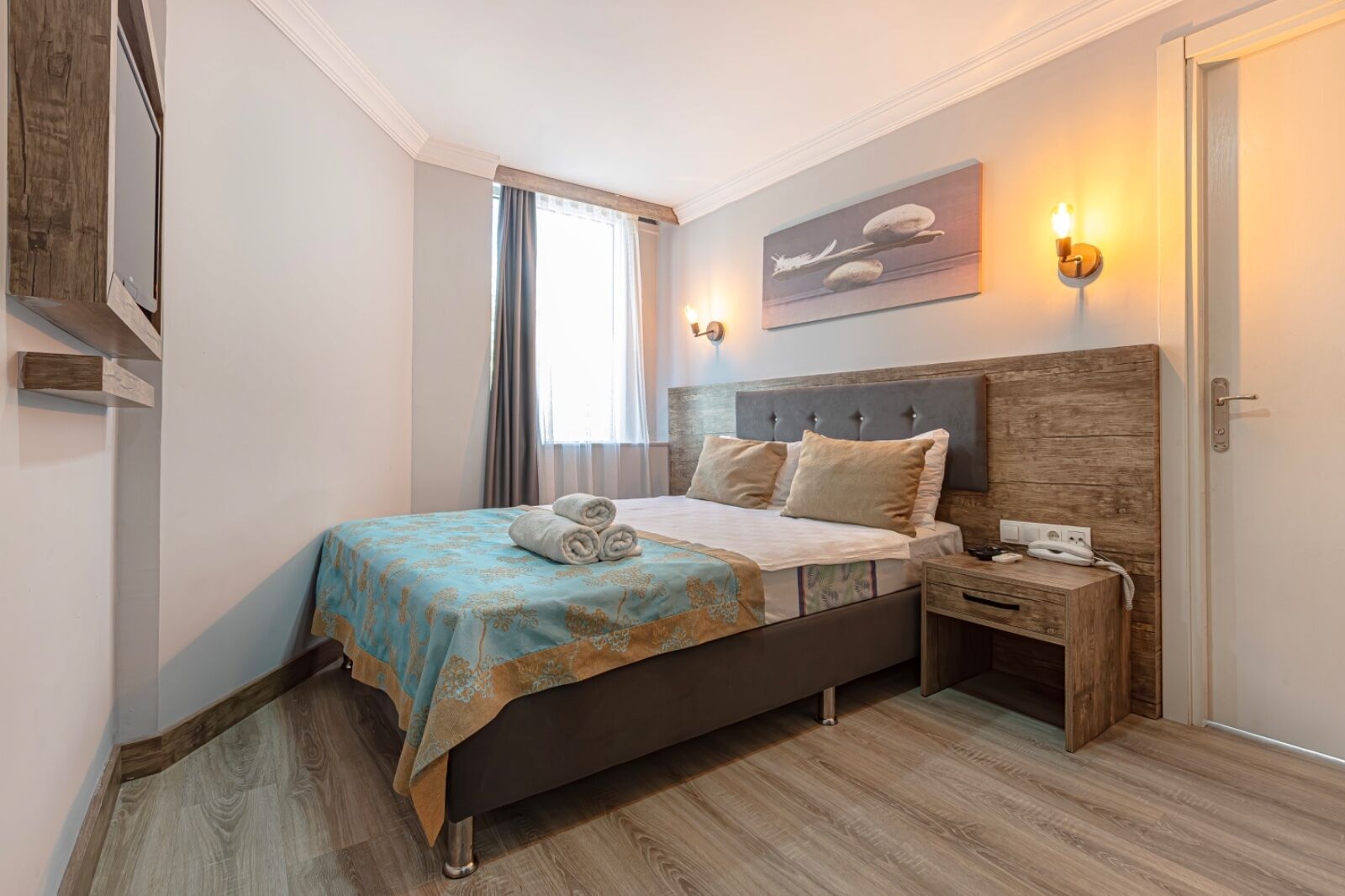 Un dormitorio con cama, mesita de noche, lámpara y una obra de arte en la pared.