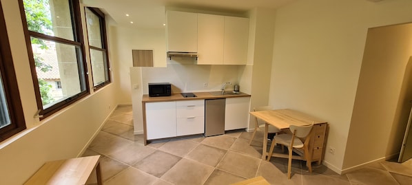 A compact kitchen with a microwave, sink, and wooden table. - Grand Studio Neuf Climatise Intramuros 9A (Avignon)