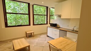 A compact kitchen with two windows, a microwave, a sink, and a small table. - Grand Studio Neuf Climatise Intramuros 9A (Avignon)