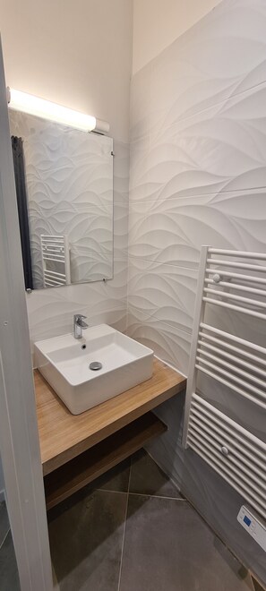 A modern bathroom with a white sink, wooden vanity, and a wall-mounted towel rack. - Grand Studio Neuf Climatise Intramuros 9A (Avignon)