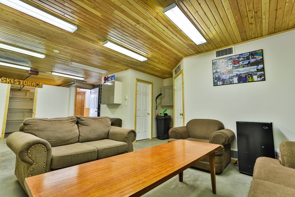 A room with a wooden ceiling, a sofa, a table, and a refrigerator.