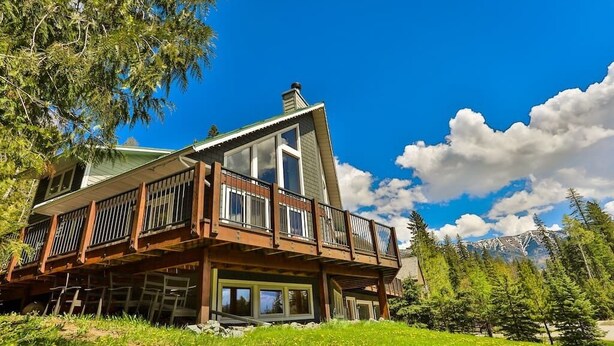 A two-story lodge with a balcony, surrounded by a forest and mountains.