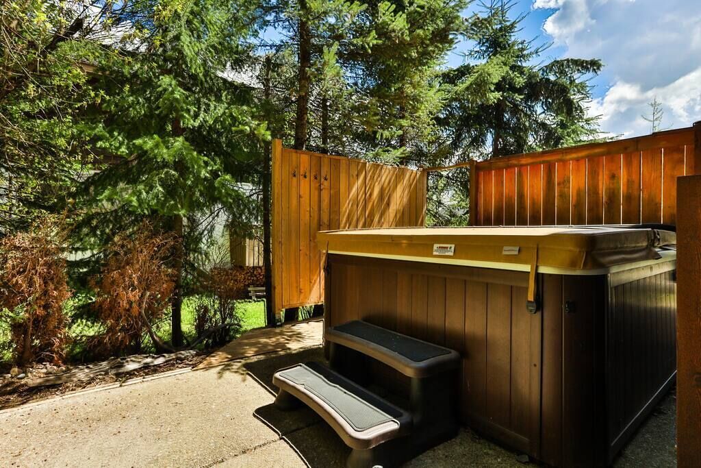 Un bain à remous doté d’une terrasse en bois et d’un marchepied en métal, entouré d’une clôture en bois et d’arbres.