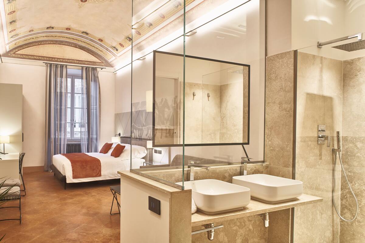 A modern hotel room with a large bed, a glass-enclosed shower, and a large mirror.