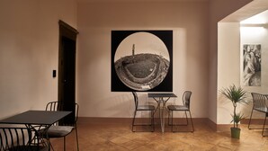 A dining area with a table and chairs, a large framed artwork on the wall, and a potted plant.