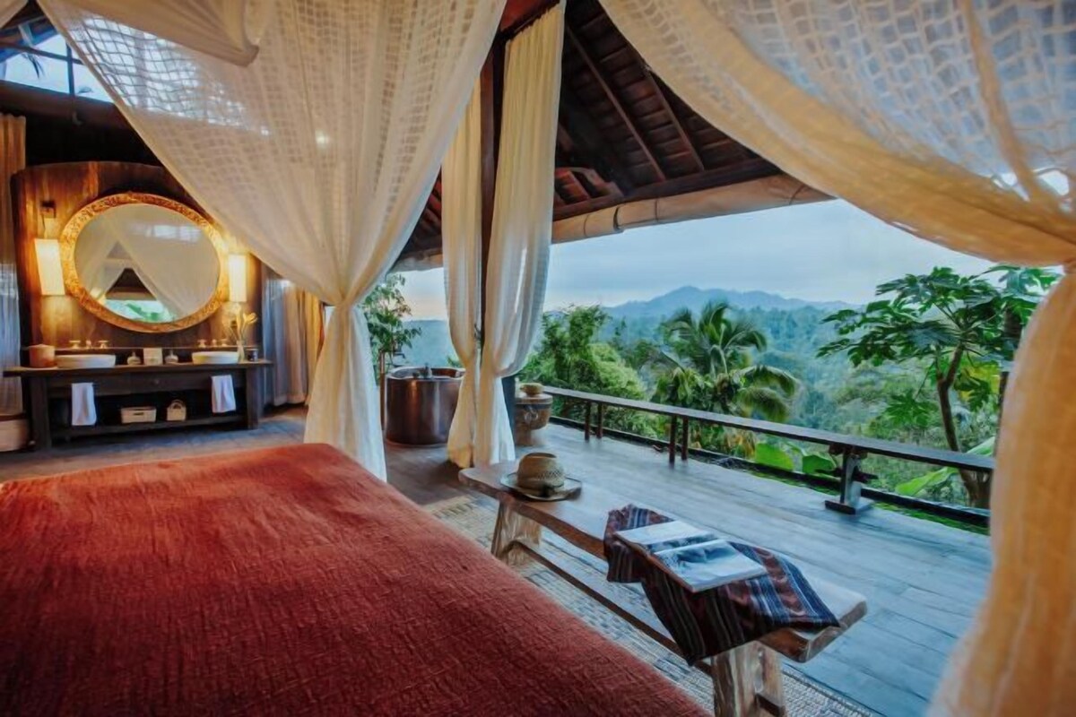 Un dormitorio con cama, mesita de noche, espejo y vistas al exterior.