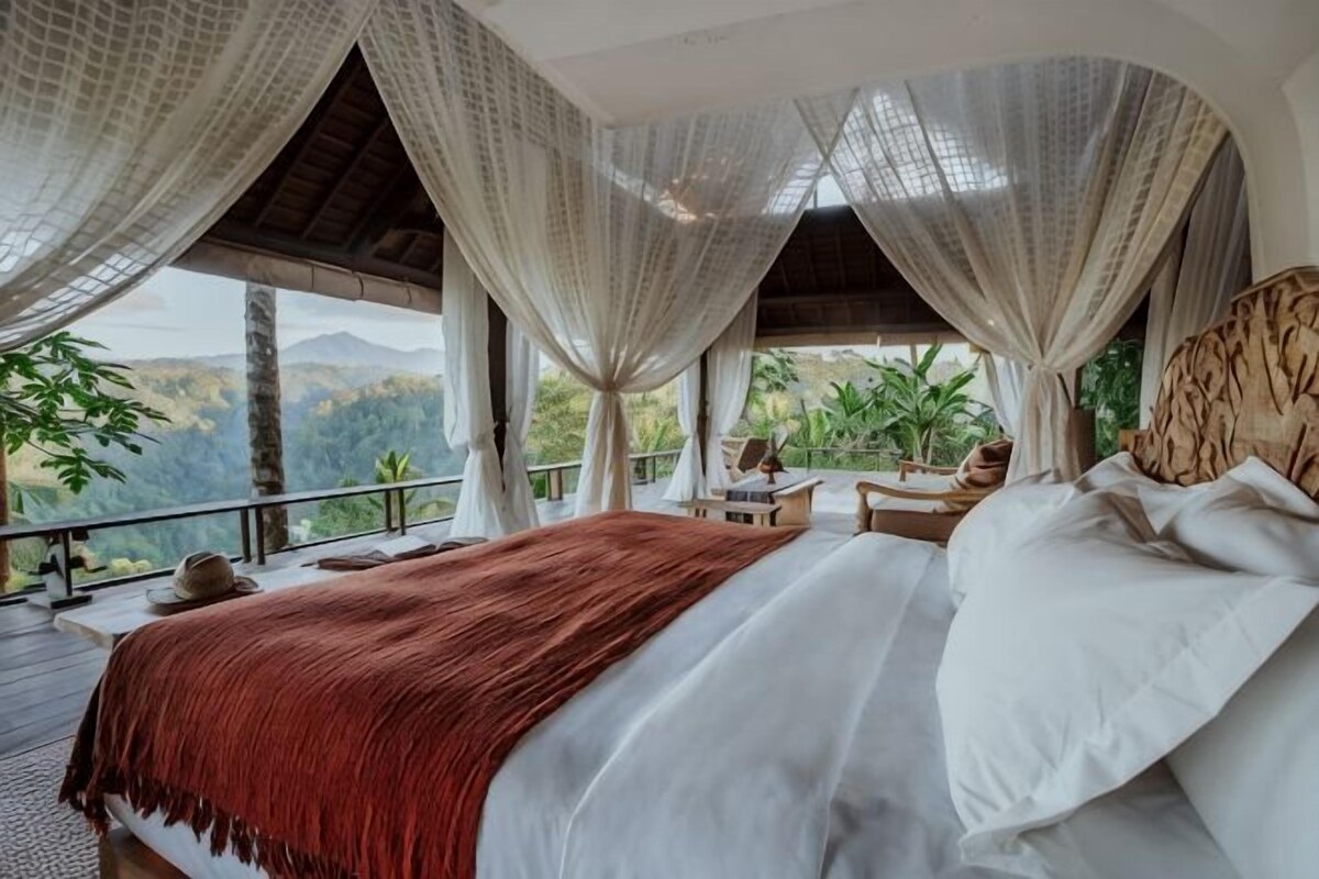 A bedroom with a bed, curtains, and a view of the outdoors.