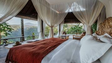 Ein Schlafzimmer mit einem großen Bett, weißen Leinen, einer roten Decke und durchsichtigen Vorhängen.