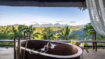 A bathtub with a view of mountains and greenery.