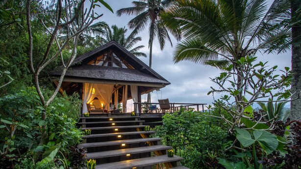 A wooden staircase leading to a building surrounded by lush greenery and palm trees. - Buahan, A Banyan Tree Escape (Payangan)