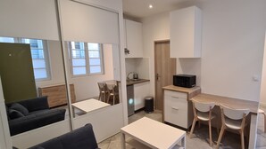 Un espace de vie compact comprenant un coin cuisine, un coin repas avec deux chaises, un canapé et une petite table.