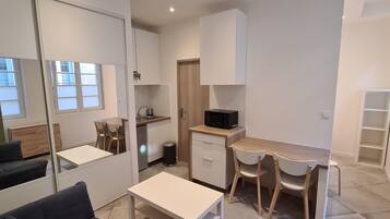 Een compacte leefruimte met kitchenette, een eethoek met twee stoelen, een bank en een kleine tafel.