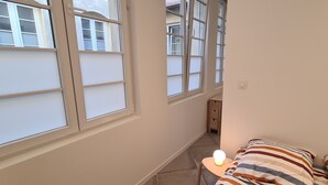 Un couloir étroit doté de grandes fenêtres, un lit avec une literie à rayures et une table de chevet avec une lampe.