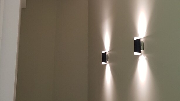 Une pièce avec un mur de couleur beige sobre, un plafond blanc doté d’un éclairage encastré et un petit objet noir accroché au mur.