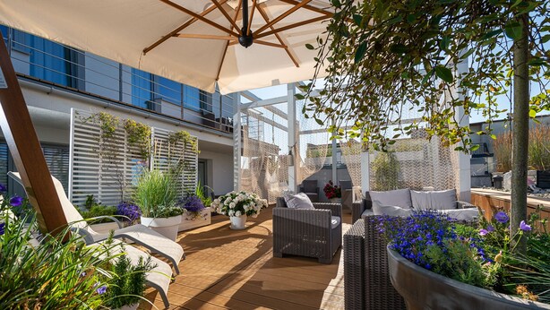 A sunlit outdoor patio with wicker furniture, potted plants, and a large umbrella. - Elegante Apartments - Adults only (Wladyslawowo)