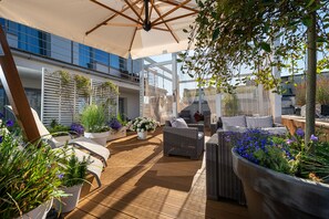 A sunlit outdoor patio with wicker furniture, potted plants, and a large umbrella. - Elegante Apartments - Adults only (Wladyslawowo)