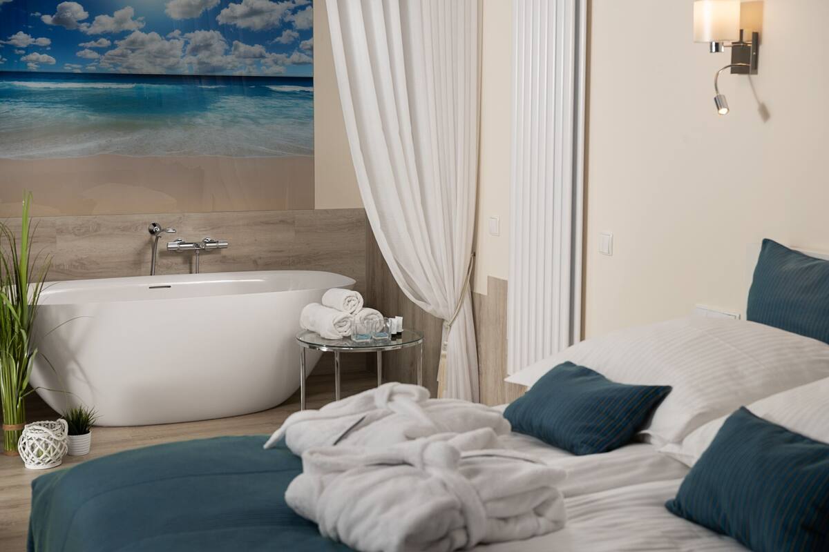 A modern hotel room with a large bed, a bathtub, and a view of the ocean.