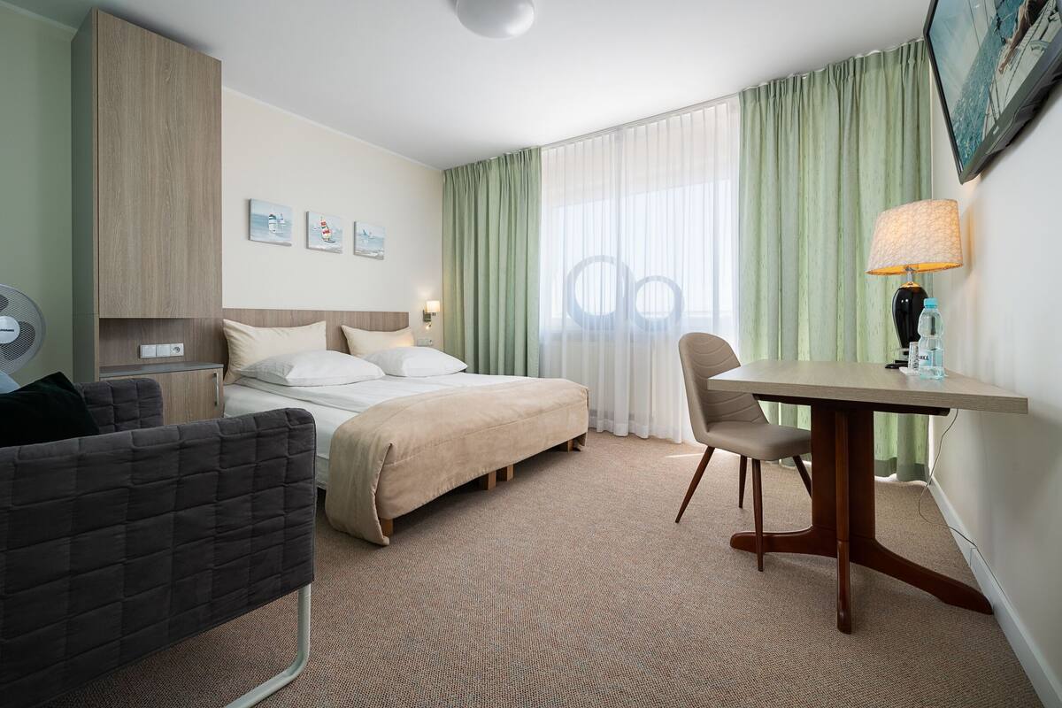 A hotel room with a bed, a desk, a chair, a fan, and a TV on the wall.