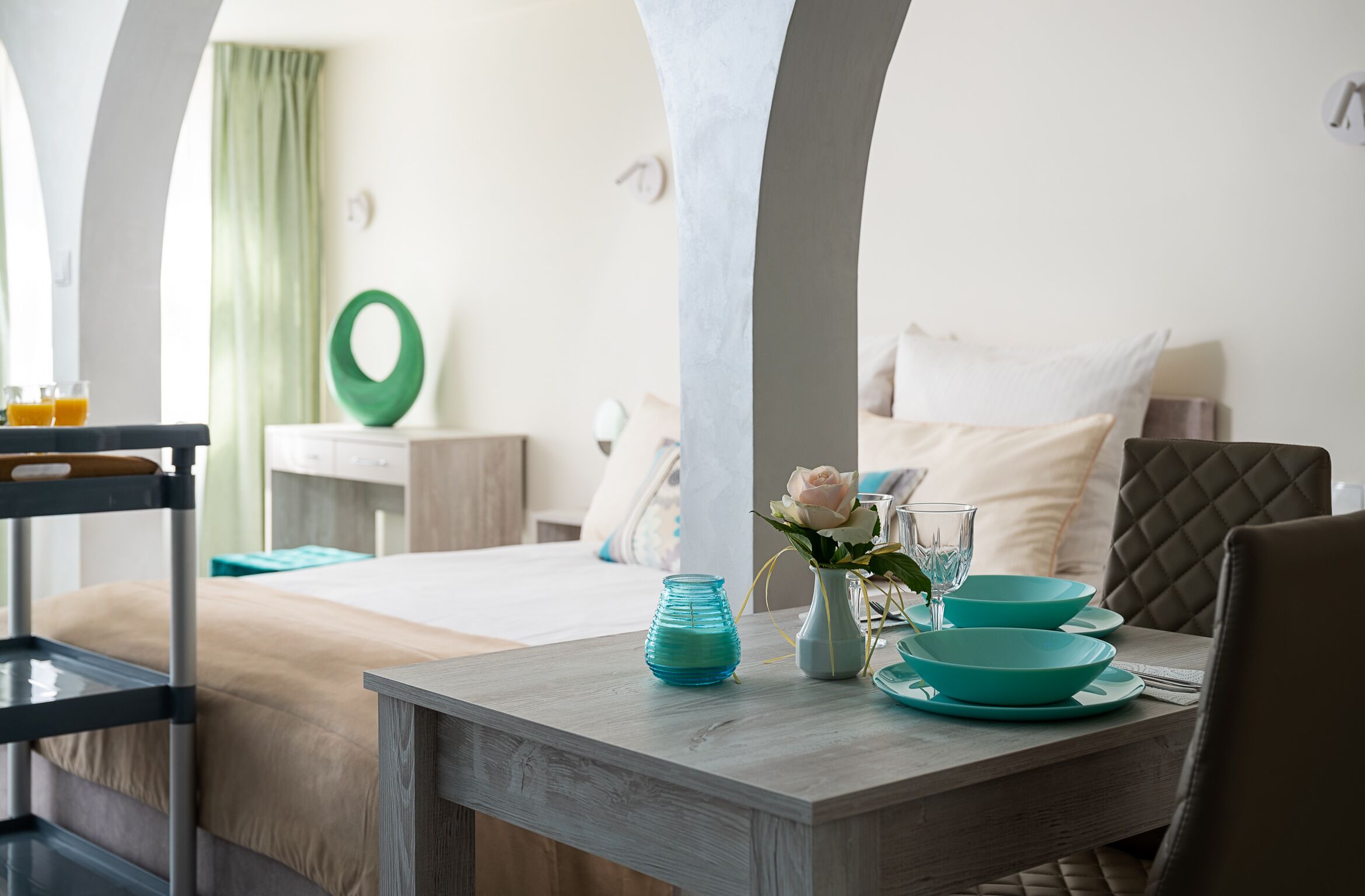 A dining area with a wooden table, teal plates, and a vase with a flower.