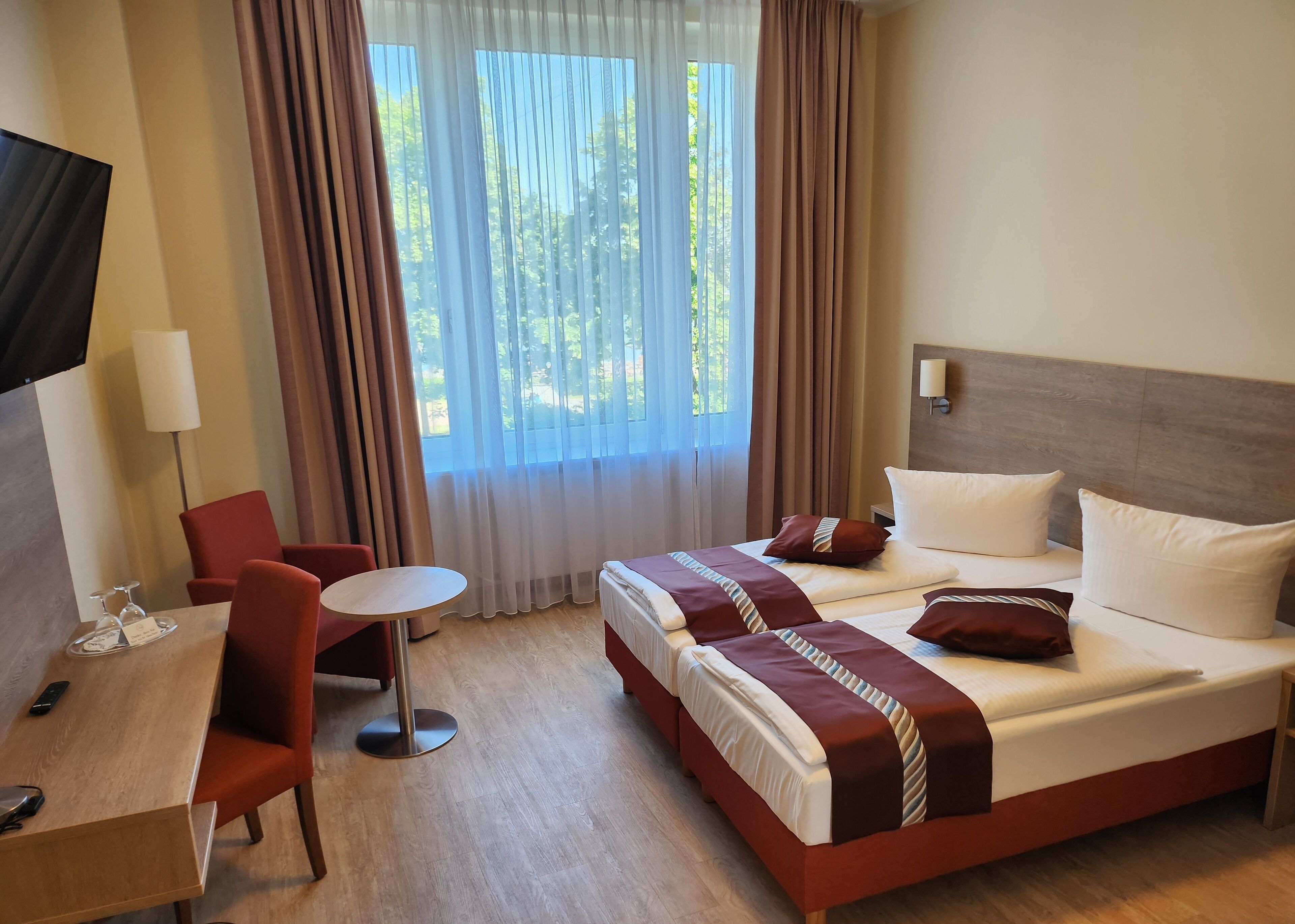 Ein Hotelzimmer mit einem Bett, einem Schreibtisch mit Stuhl, einem Fernseher und einem Fenster mit Vorhängen.