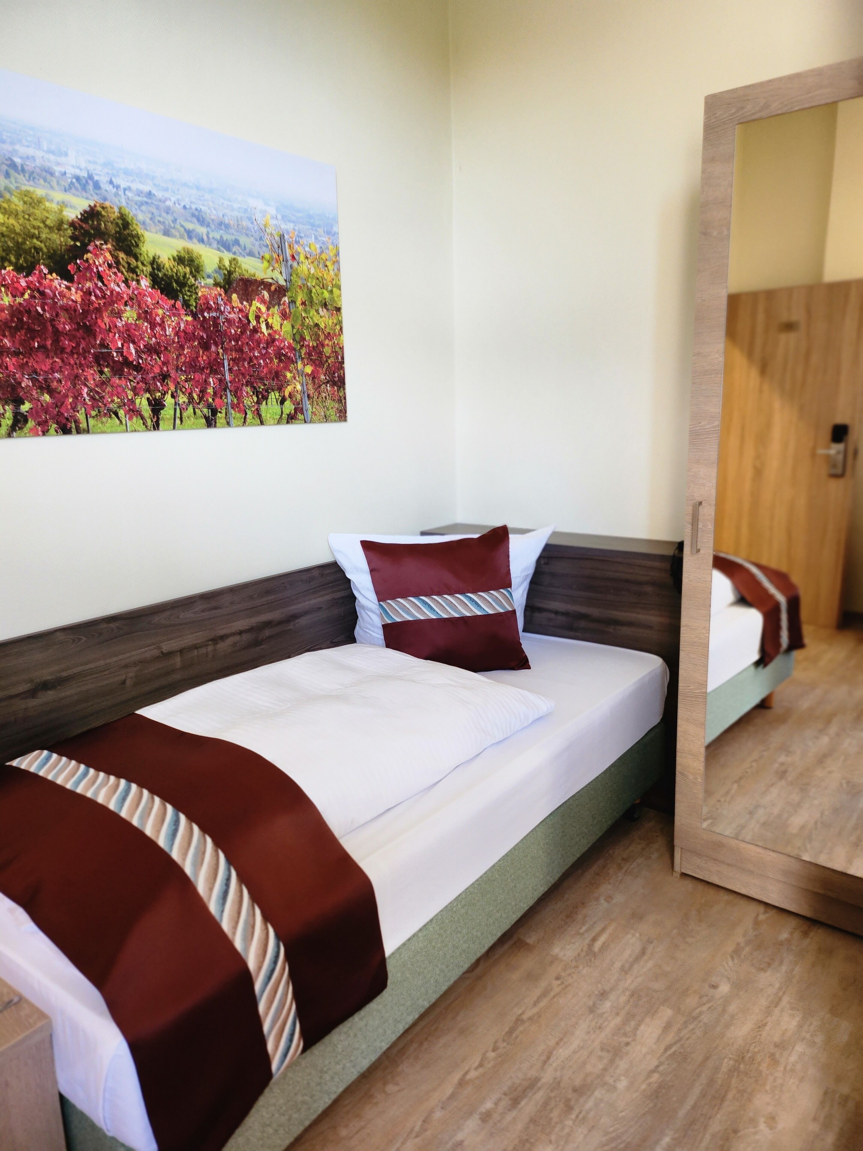 Una cama bien hecha con sábanas blancas y dos almohadas, un cabecero de madera y un cuadro grande de un paisaje en la pared.