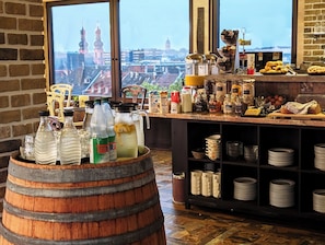 Una barra de desayuno con vista a un paisaje urbano, que incluye un barril de madera, botellas, frascos y una variedad de alimentos para el desayuno.