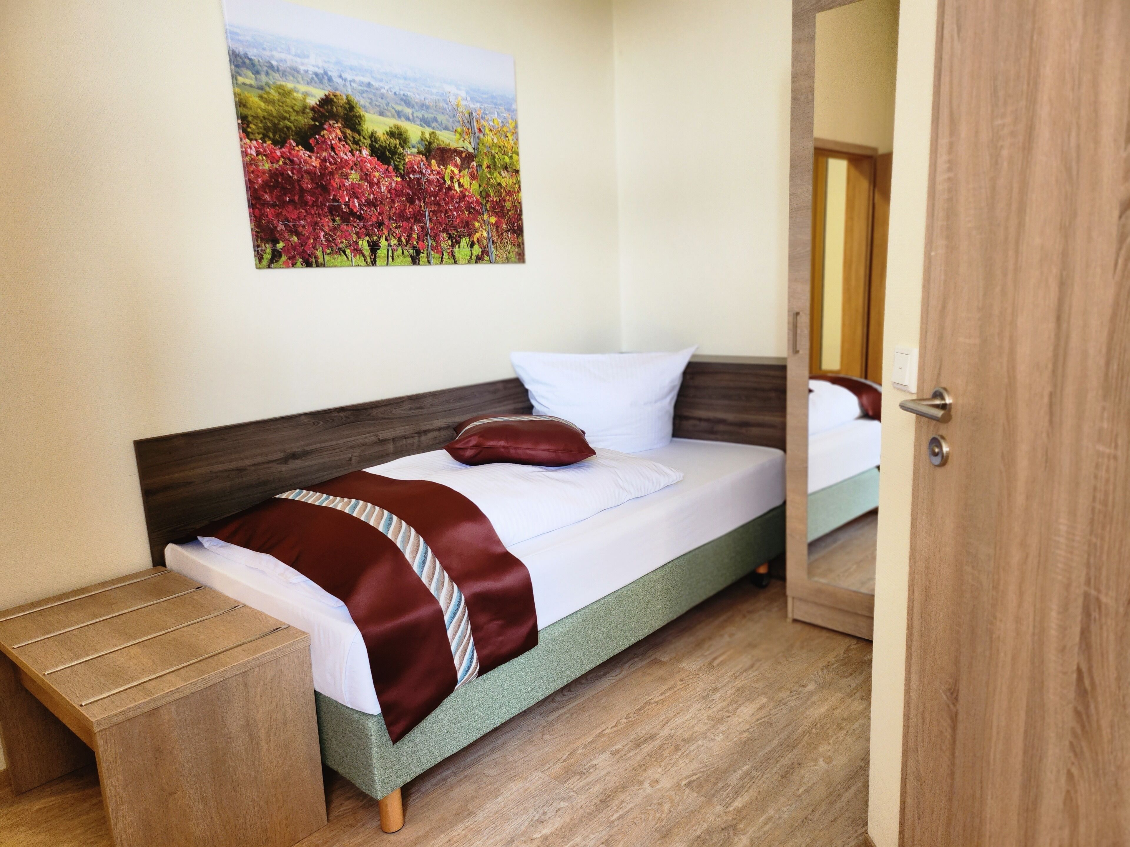 Ein Schlafzimmer mit Bett, Nachttisch, Holztür und einem Landschaftsbild.