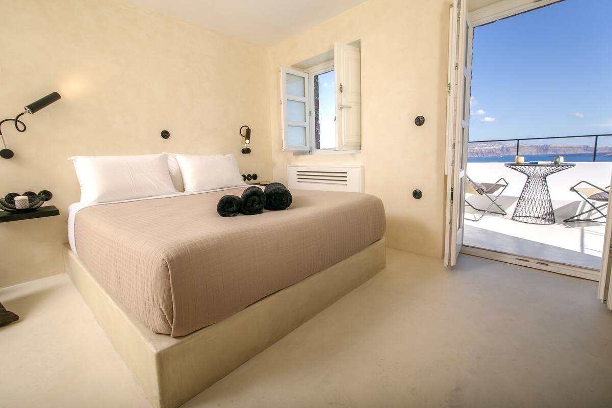 A bedroom with a large bed, a bedside table, a mirror, and a view of the balcony.