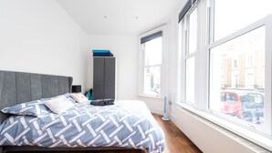 A modern bedroom with a large bed, grey wardrobe, and a window with a city view. - Gorgeous Apartment by the Park (SS2) (Greater London)
