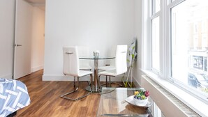 A modern room with a glass table, white chairs, and a view of the city through large windows. - Gorgeous Apartment by the Park (SS2) (Greater London)
