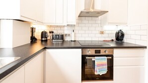 A modern kitchen with white cabinets, a black countertop, a built-in oven, and a range hood. - Gorgeous Apartment by the Park (SS2) (Greater London)