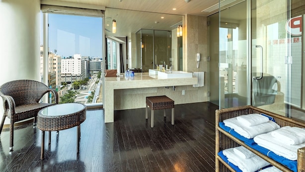 Un baño moderno con un espejo grande, un lavabo y un inodoro. Hay una silla de mimbre y una mesita con toallas.