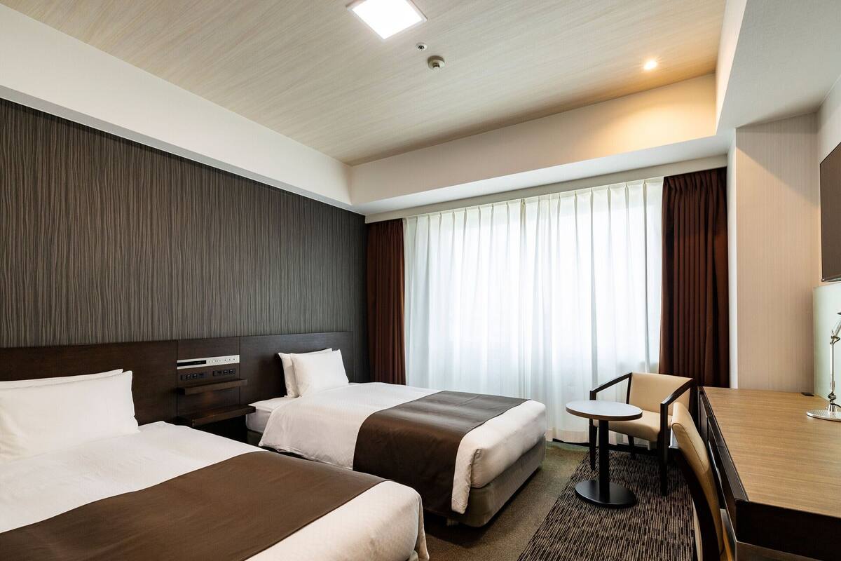 A hotel room with two beds, a desk, and a chair.