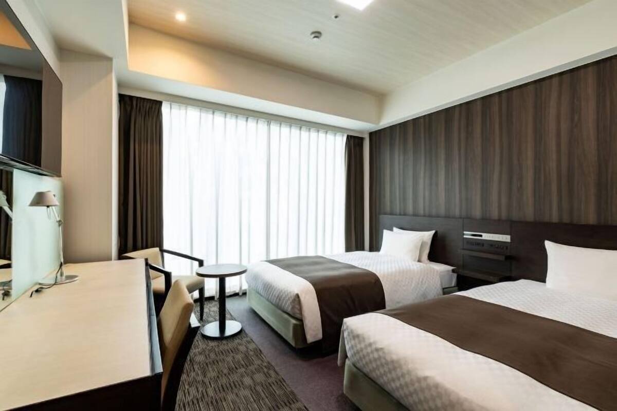 A hotel room with two beds, a desk, a chair, and a small table.