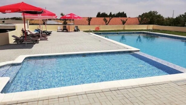 A swimming pool with lounge chairs and red umbrellas. - Nefama Blue Pensão Apt5 (Ourique)