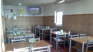 A classroom with desks and chairs arranged in rows, a television mounted on the wall, and a window providing natural light. - Nefama Blue Pensão Apt5 (Ourique)