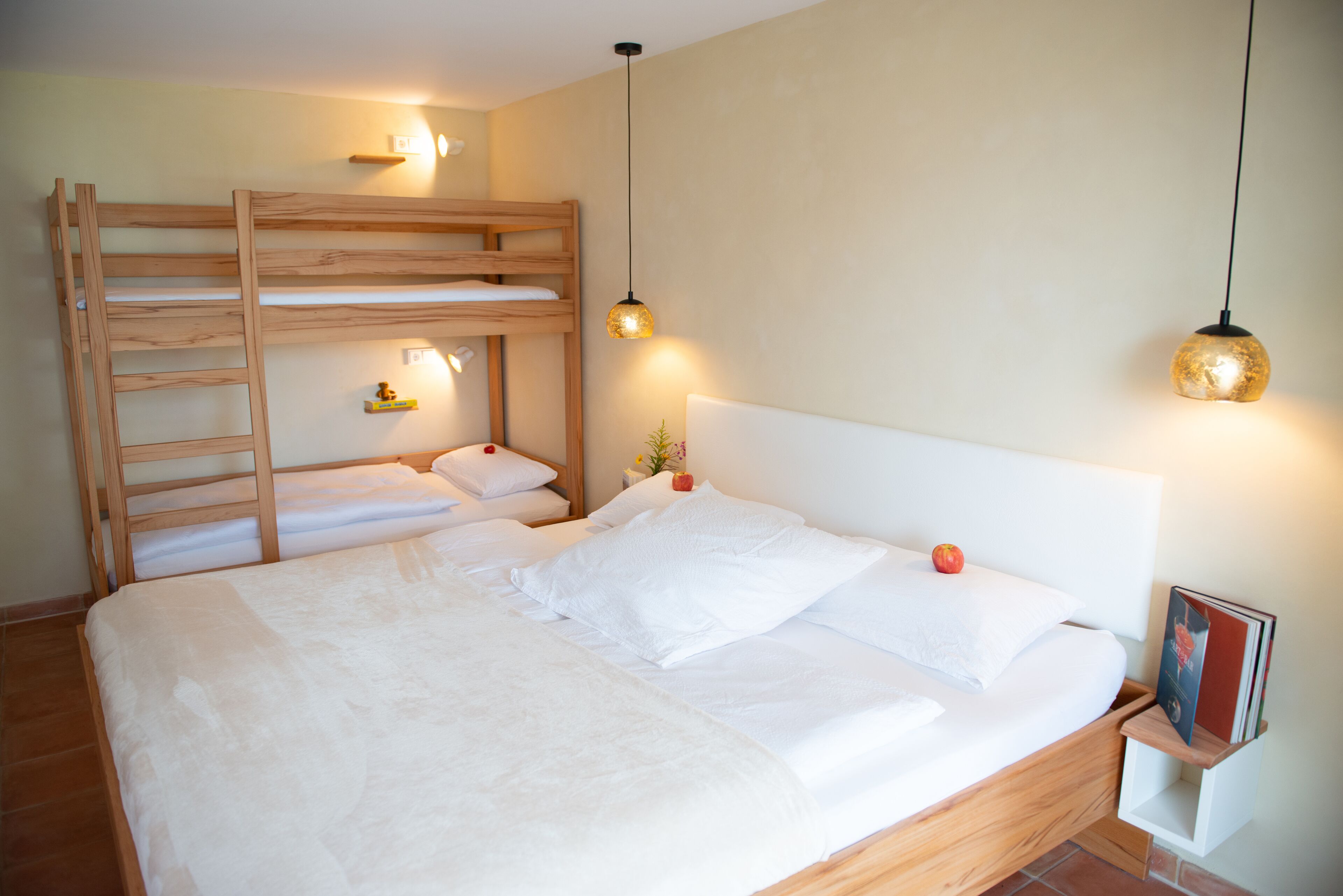 Uma cama beliche com escada de madeira, uma mesa de cabeceira com abajur e um quadro emoldurado no criado-mudo.