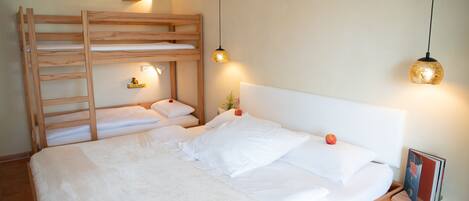 Uma cama beliche com escada de madeira, uma mesa de cabeceira com abajur e um quadro emoldurado no criado-mudo.
