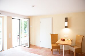 A dining area with a table and chairs, a white door, and a window with a view of greenery. - Gartenappartement in der Finca / Spanische Rhön (Hünfeld)