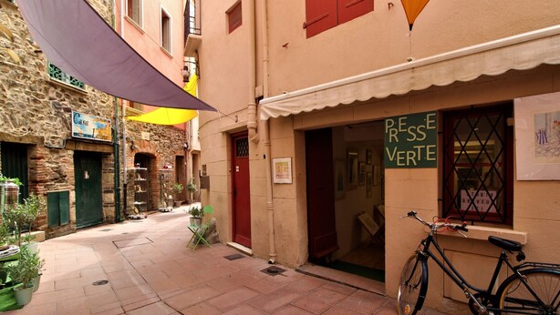 Une rue étroite où est garé un vélo devant un immeuble sur lequel on peut lire l’inscription « PRESSE VERTE ».