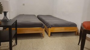 Une petite chambre avec deux lits simples, un bureau avec une chaise et une lampe.