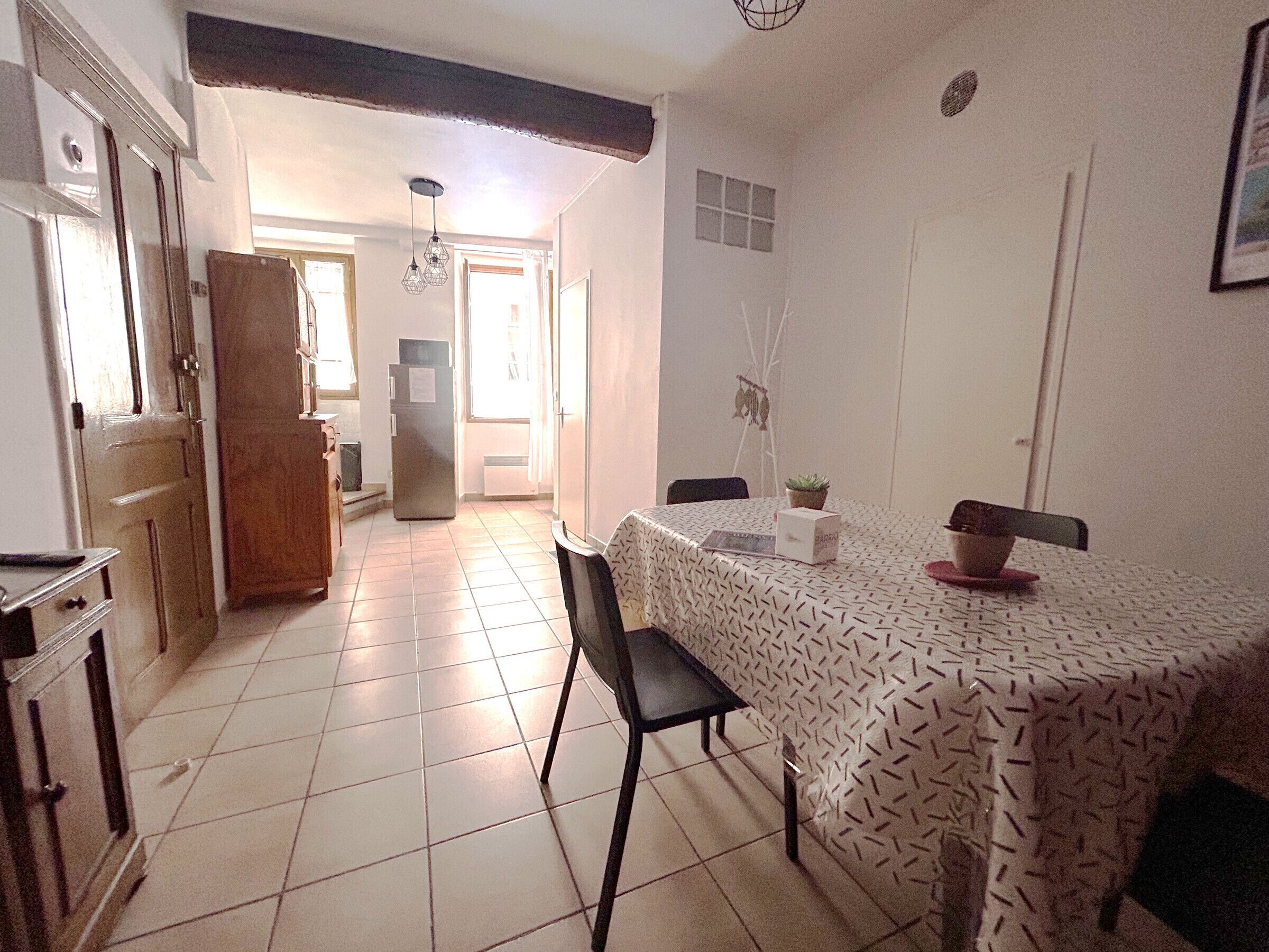 A dining area with a patterned tablecloth, a refrigerator, and a chair.