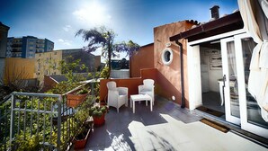 Eine Terrasse mit weißen Korbmöbeln, einer Waschmaschine und Topfpflanzen.